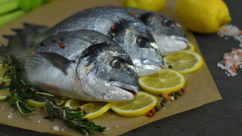 Raw fish with aromatic herbs, spices, salt and lime slices.Raw dorado on dark background, healthy food, cooking, diet, nutrition concept.Mediterranean seafood. gilt-head sea bream.Selective focus.